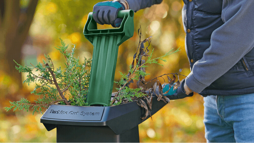 Rozdrabniacz do gałęzi BOSCH AXT 25 TC elektryczny 2500 W sekator + rękawice gród trawnik zbliżenie na lej w leju umieszczone gałęzie osoba popycha materiał za pomocą popychacza zautomatyzowany lej załadowczy materiał jest pobierany do mechanizmu cięcia automatycznie szeroka rynna szybkie podawanie odpadów praktyczny popychacz