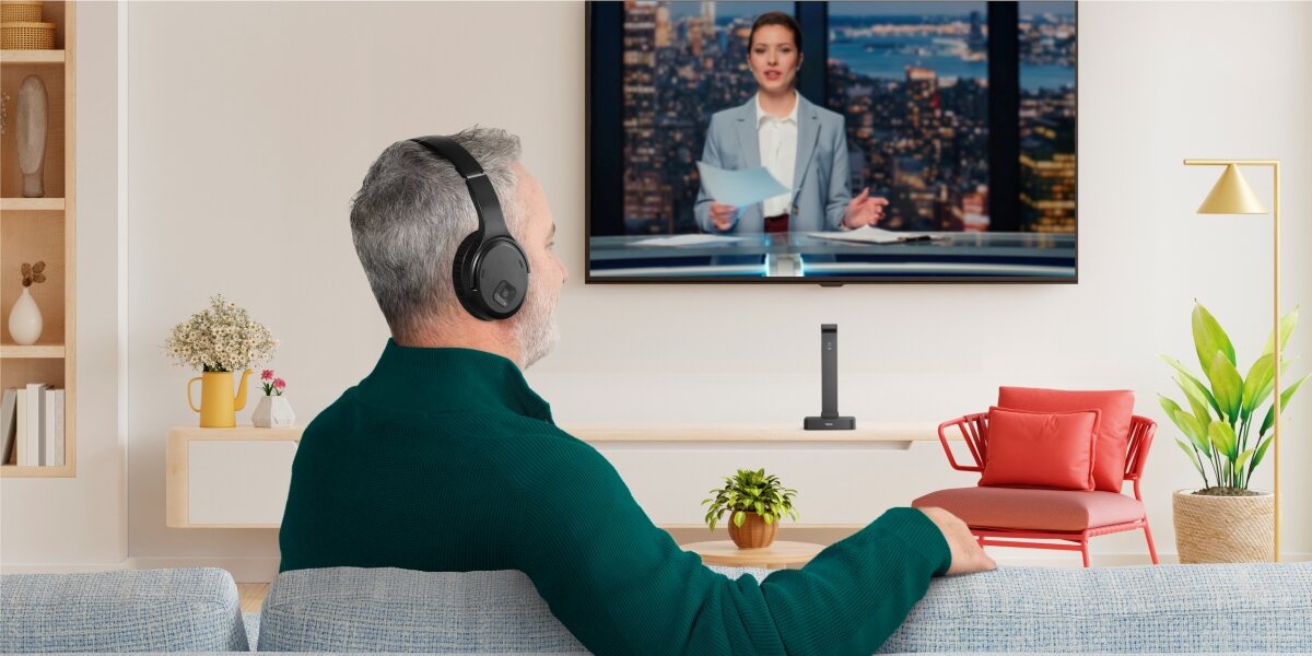 Słuchawki nauszne HAMA Over-Ear Czarny Mężczyzna w czarnych słuchawkach bezprzewodowych ogląda wiadomości na dużym telewizorze w nowoczesnym salonie.