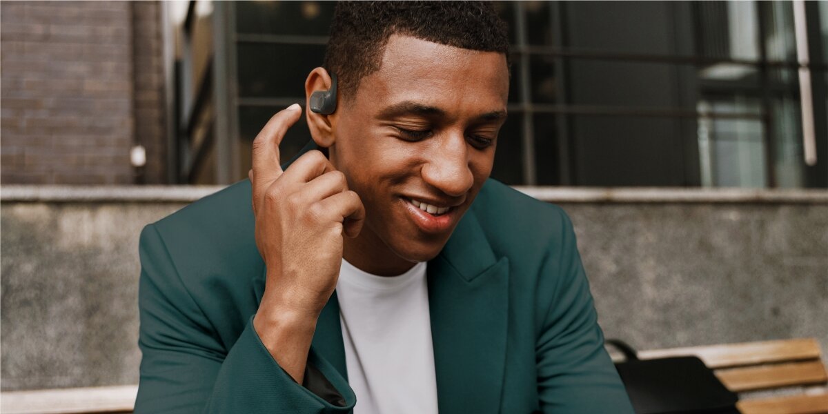 Słuchawki powietrzne HAMA Spirit Open Czarny Mężczyzna w ciemnozielonej marynarce korzysta z dousznych słuchawek sportowych z zausznikami podczas siedzenia na zewnątrz.