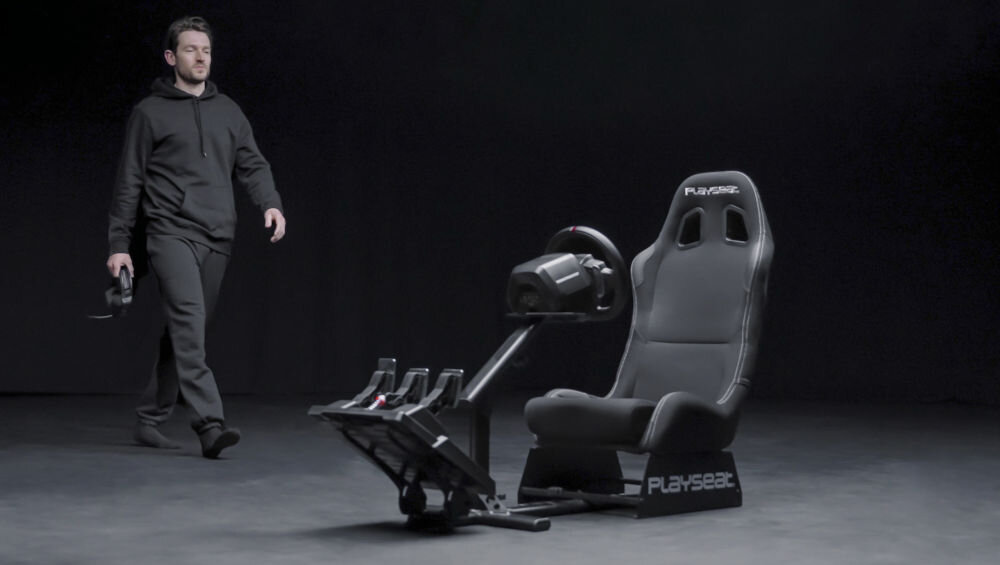 Kokpit PLAYSEAT Evolution Czarny prezentacja kokpitu z kierownicą i pedałami na ciemnym tle mężczyzna idący do niego