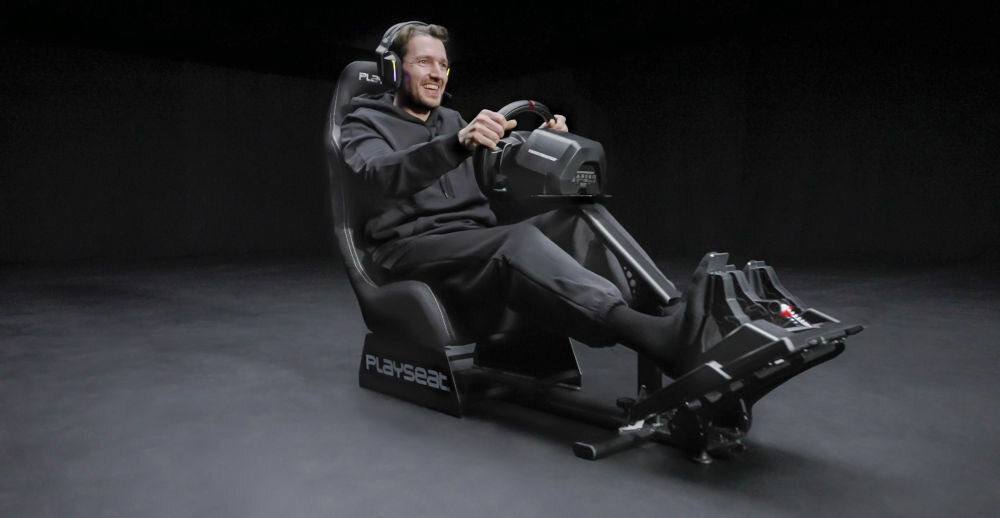 Kokpit PLAYSEAT Evolution Czarny prezentacja kokpitu z kierownicą i pedałami na ciemnym tle mężczyzna siedzący na fotelu realizm komfort kompatybilność z konsolami Playstation