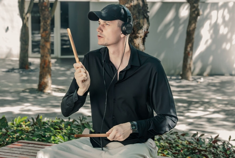  Przenośna perkusja elektroniczna AeroBand PocketDrum 2 Max – elektroniczne pałki perkusyjne, osoba z założonymi słuchawkami nausznymi oraz pałeczkami od perkusji