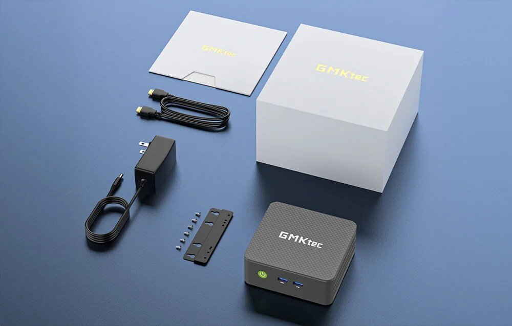 Komputer GMKTEC G3S Zestaw elementów na niebieskim tle zawierający kwadratowe urządzenie, białe pudełko, instrukcję, zasilacz, kabel oraz uchwyt montażowy ze śrubkami