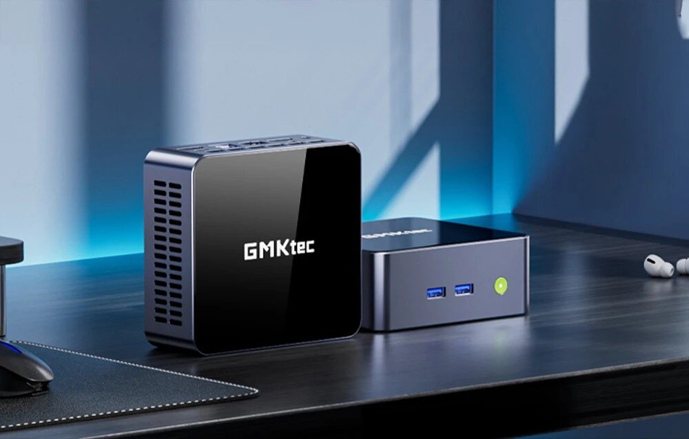 Komputer GMKtec M2 Pro S Dwa małe, ciemne komputery o błyszczącej powierzchni ustawione obok siebie na czarnym biurku w pobliżu myszki i słuchawek bezprzewodowych