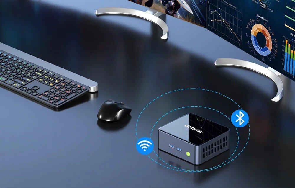 Komputer GMKtec M2 Pro S Widok na czarne biurko z klawiaturą, myszką i dwoma monitorami wyświetlającymi dane, na którym stoi małe urządzenie z ikonami Wi-Fi i Bluetooth