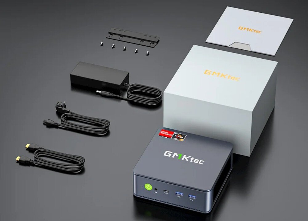 Komputer GMKTEC M6 Ultra Komplet zawartości pudełka mini PC z czarną obudową, kablami zasilającymi i HDMI, uchwytem montażowym oraz dwoma białymi pudełkami z logo GMKtec w kolorze pomarańczowym