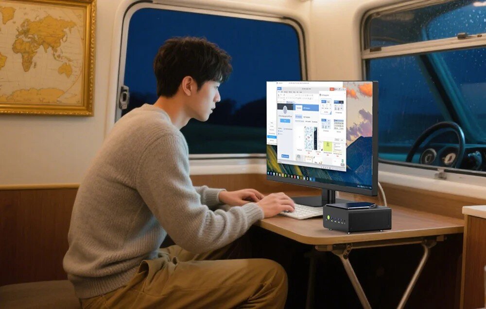 Komputer GMKTEC NucBox K12 Mężczyzna pracujący przy biurku wewnątrz kampera lub pociągu, korzystający z komputera podłączonego do monitora