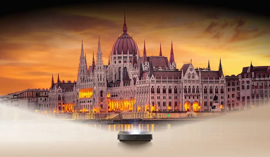 Projektor laserowy Hisense wyświetlający na ścianie budynek Parlamentu w Budapeszcie na tle zachodzącego słońca.