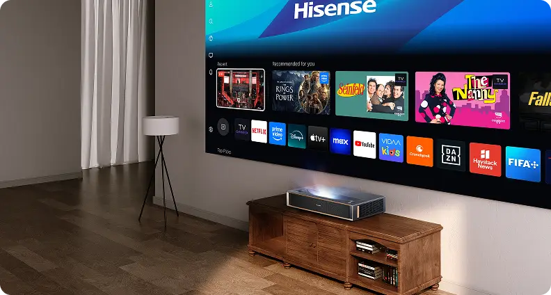Projektor na szafce rzuca na ścianę interfejs Hisense z kafelkami filmów i ikonami aplikacji: Netflix, Prime Video i YouTube.
