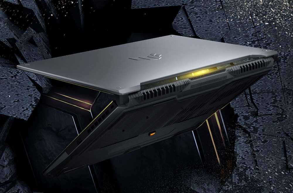 ASUS TUF Gaming F16 w pozycji półotwartej na ciemnej kamienistej powierzchni z żółtymi akcentami świetlnymi, demonstrujący certyfikację MIL-STD 810H z 12 metodami testów militarnych odporności na wstrząsy, temperatury ekstremalne i wilgotność dla niezawodności w każdych warunkach - MIL-STD-810H 