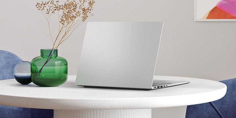 Laptop ASUS VivoBook S 16 na stole obok wazonu z kwiatami.   - Wzornictwo metaliczne wykończenie 