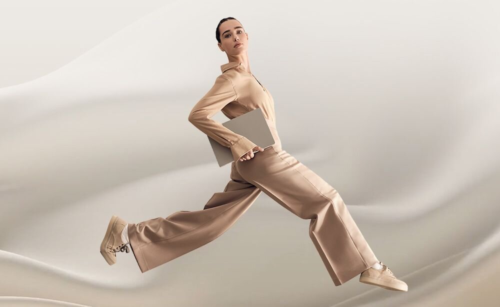  Kobieta w beżowym stroju biegająca z laptopem ASUS Zenbook w ręku na minimalistycznym tle, podkreślenie ultralekkiej konstrukcji ważącej zaledwie 980 gramów - Lekka konstrukcja 980 gramów 