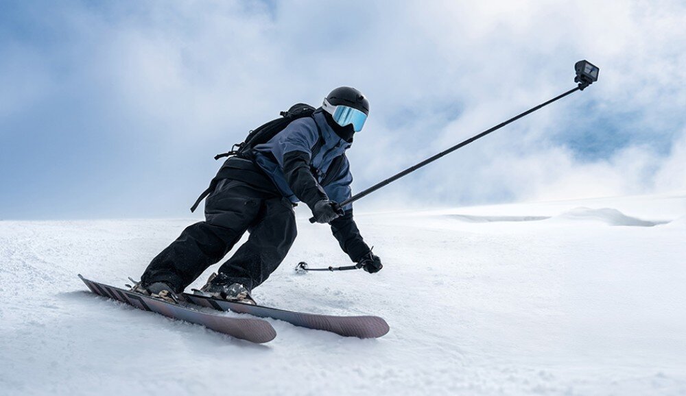 Kamera sportowa DJI Osmo Action 6 Narciarz w pełnym ekwipunku zjeżdżający po stoku z kamerą na kasku, zestaw, dodatki