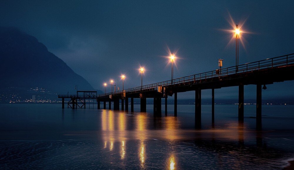 Kamera sportowa DJI Osmo Action 6 Oświetlone molo nocą odbijające się w spokojnej tafli wody, zmienna przesłona, oświetlenie, tryb Auto