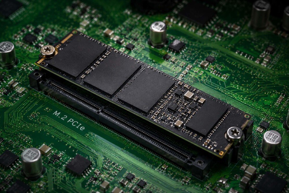 Komputer All in One ACER Aspire C24-2YE13U5UNL Widok z bliska na dysk SSD typu M.2 PCIe przykręcony do zielonej płyty głównej komputera, widoczne są czarne układy scalone oraz metalowe elementy montażowe, dysk, pojemność