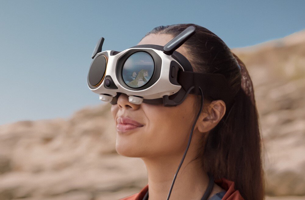 Dron ANTIGRAVITY A1 Uśmiechnięta kobieta w goglach patrząca w górę na tle rozmytych skał, proporcje