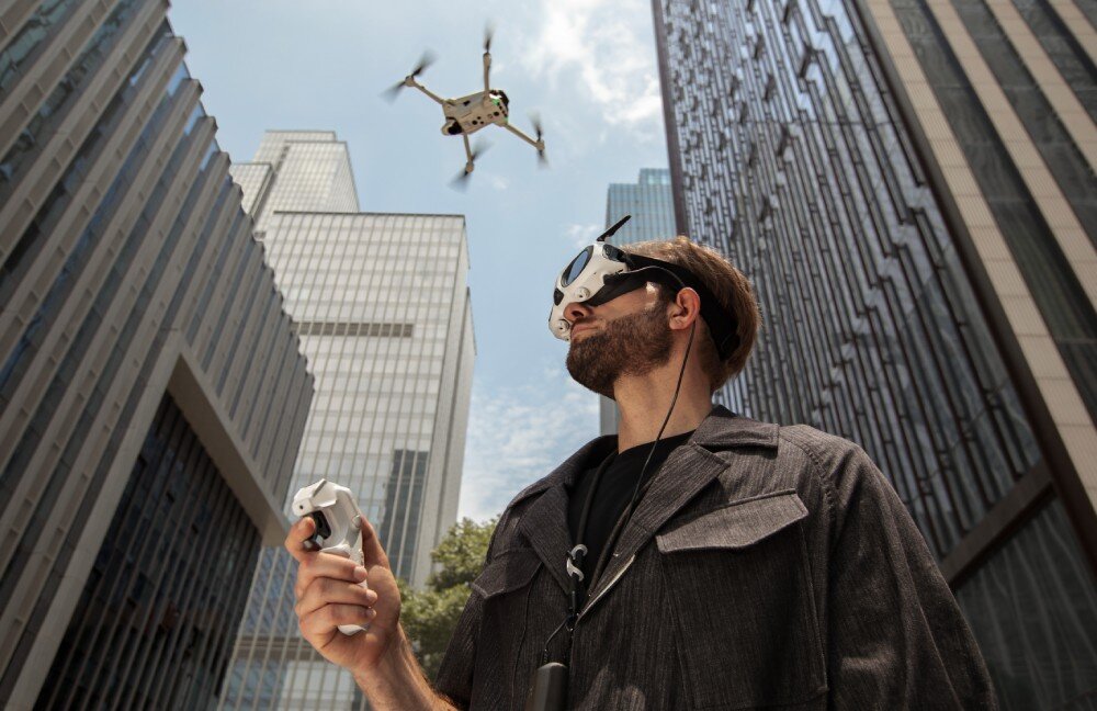 Dron ANTIGRAVITY A1 Mężczyzna w goglach steruje dronem w przestrzeni miejskiej między wieżowcami, przednie czujniki, wykrywanie przeszkód, wymiana soczewek