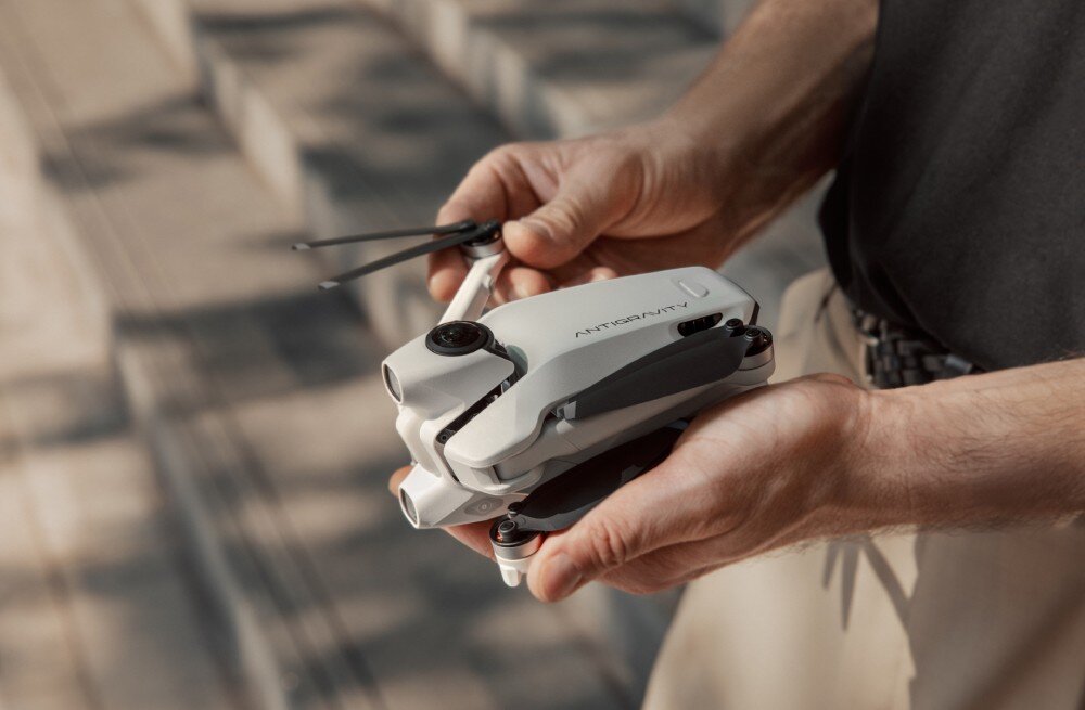 Dron ANTIGRAVITY A1 Dłonie trzymające złożonego kompaktowego drona w kolorze białym, materiały 360, kadry