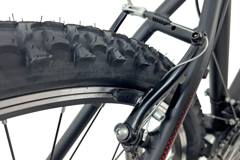 Zbliżenie na tylne koło roweru górskiego z widocznym bieżnikiem opony i hamulcem typu V-brake. Na ramieniu hamulca widoczny jest napis \'Saccon\'.