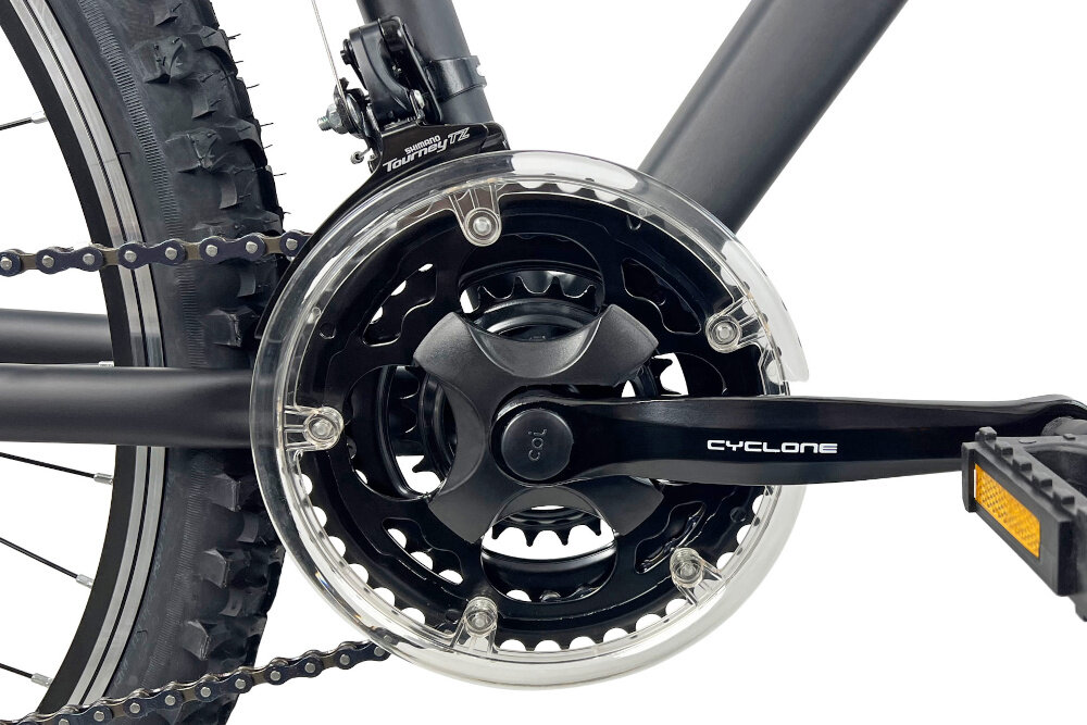 Zbliżenie na mechanizm korbowy roweru z napisem \'CYCLONE\' na ramieniu korby. Widoczna jest także część opony z wyraźnym bieżnikiem oraz przerzutka z napisem \'Shimano Tourney TZ\'.