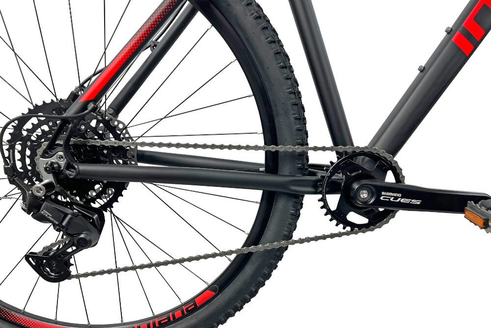 Zbliżenie na tylne koło roweru górskiego z widocznym mechanizmem napędowym i przerzutką. Na ramieniu korby widoczny napis \'Shimano Cues\'.