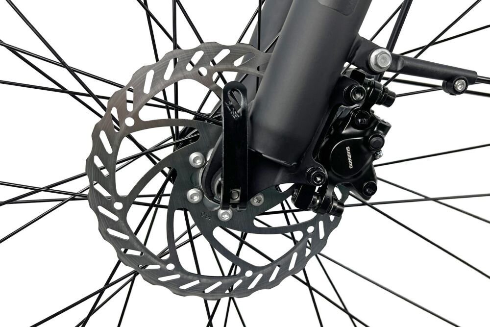 Zbliżenie na tarczę hamulcową roweru z widocznym zaciskiem hamulcowym marki Shimano. Tarcza jest metalowa z otworami, a zacisk jest czarny.