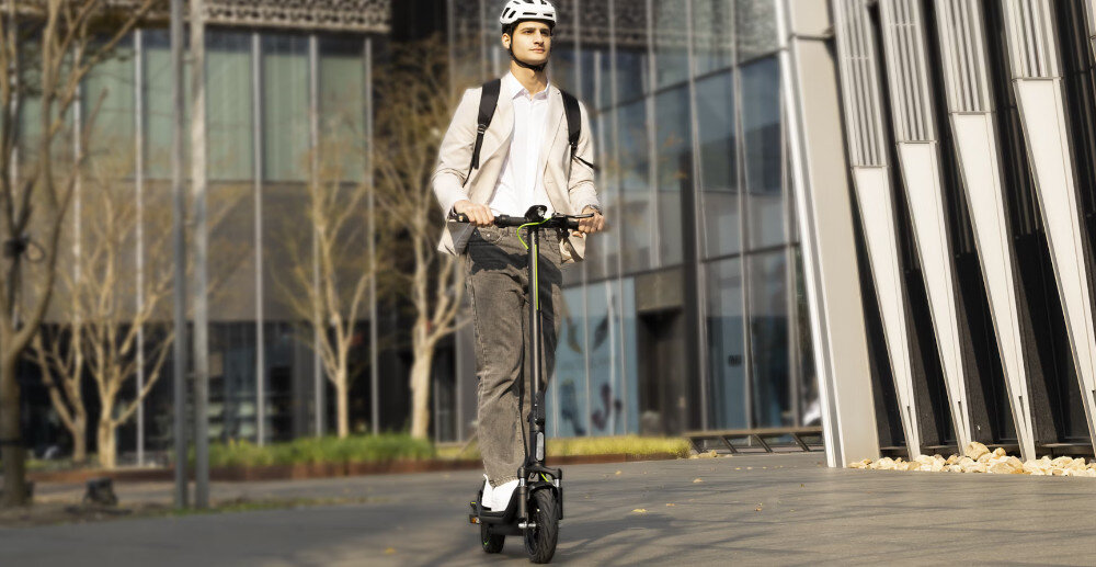 Hulajnoga elektryczna ACER ES Series 5 Select 60km 500W Amortyzacja 10 cali Czarny miasto droga osoba jedzie na hulajnodze po mieście w tle szklane budynki do jazdy po mieście szereg udogodnień i praktycznych rozwiązań moduł Bluetooth kierunkowskazy składana konstrukcja styl moc wygoda