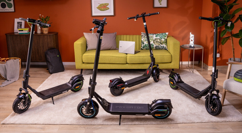 Hulajnoga elektryczna ACER ES Series 5 Select 60km 500W Amortyzacja 10 cali Czarny pokój cztery hulajnogi ustawione na podłodze każda opiera się na stopce w tle pomarańczowa ściana żółta kanapa komoda kwiat składana stopka wytrzymała nóżka zamontowana w centralnym punkcie ciężkości zapobiega przypadkowemu przewróceniu się pojazdu