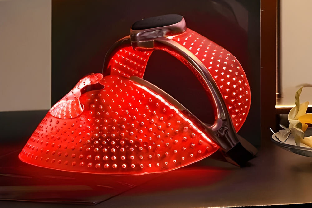 Maska LED FOREO Faq 202 Szeroki kąt ujęcia maski LED złożonej na stole, cała powierzchnia maski świeci jasnym czerwonym światłem.
 