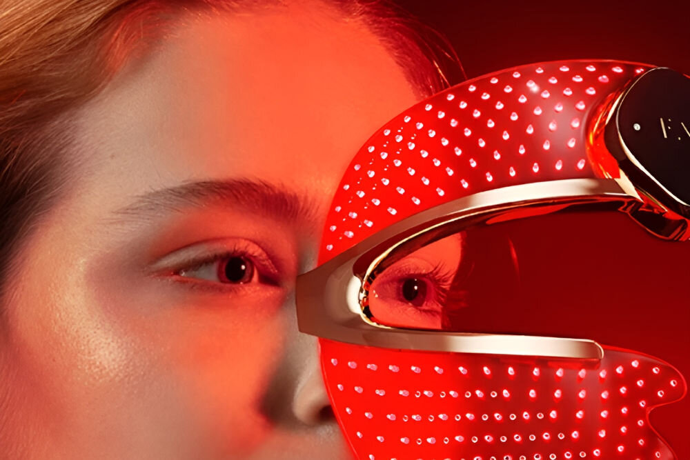 Maska LED FOREO Faq 202 Ekstremalne zbliżenie na oko kobiety i boczną część maski LED. Odbicie światła z czerwonej maski LED jest widoczne na powierzchni oka i skóry, a przez jej otwór widać część twarzy kobiety.
 