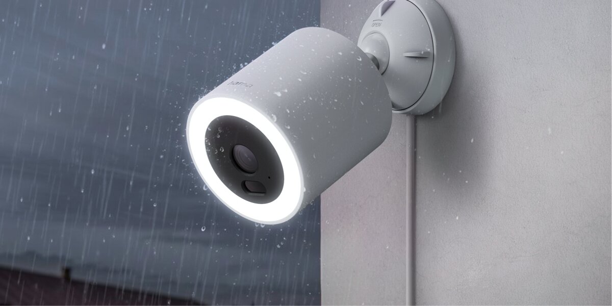 Kamera HAMA Smart Surveillance Zewnętrzna, Wi-Fi Wodoodporna kamera zewnętrzna Hama Smart Home z włączonym reflektorem LED pracująca podczas opadów deszczu.