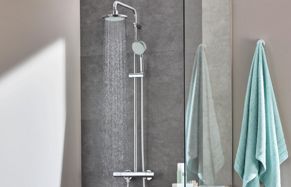 SYSTEM PRYSZNICOWY GROHE NEW TEMPESTA COSMOPOLITAN 27922000 CHROM Zdjęcie przedstawia elegancki zestaw prysznicowy z dużą deszczownicą i dodatkową słuchawką zamontowaną na regulowanej szynie. Strumień wody spływa równomiernie z górnej głowicy, podkreślając komfortowy, obfity natrysk