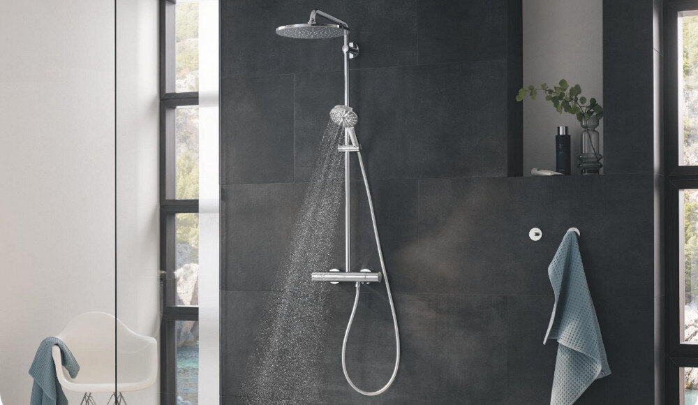 SYSTEM PRYSZNICOWY GROHE RAINSHOWER SMARTACTIVE 26647000 CHROM Zdjęcie przedstawia zestaw prysznicowy z dużą deszczownicą, z której wypływa równy, delikatny strumień wody. Na ścianie widoczna jest także dodatkowa słuchawka prysznicowa oraz miękki ręcznik zawieszony obok