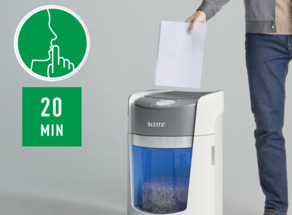 Osoba wkłada kartkę papieru do niszczarki marki LEITZ z przezroczystym pojemnikiem na ścinki. Obok widoczna jest zielona ikona z symbolem ciszy i napisem \'20 MIN\'.