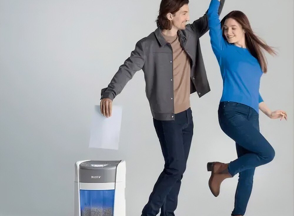 Niszczarka LEITZ IQ OptiMax Home Office 225 P5 Półzbliżenie na białą niszczarkę z niebieskim zbiornikiem wypełnionym pociętym papierem, i parą tańczącą obok niej