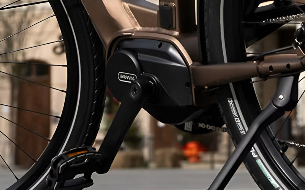 Rower elektryczny ROMET E-Modeco URB 2.0 U17 28 cali Brązowo-czarny zbliżenie na silnik widok z boku w tle budynek widoczny napis BAFANG wytrzymały, bezszczotkowy silnik marki BAFANG M200 65 Nm silnik o mocy 250 W cicha i wydajna praca umiejscowienie centralne