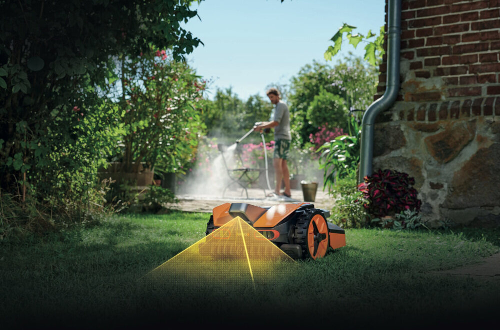Robot koszący WORX Landroid Vision WR202E robot na trawie w tle osoba myje krzesło ogrodowe drzewa dom do samodzielnego utrzymywania trawnika w małych ogrodach o powierzchni do 250 m² automatyczne koszenie oszczędność czasu dba o równą długość źdźbeł
