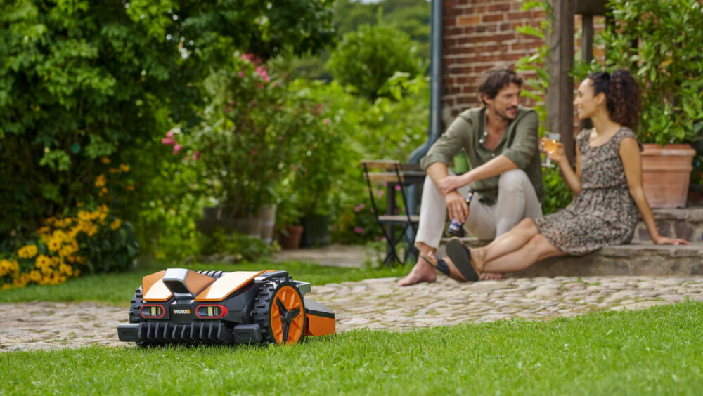 Robot koszący WORX Landroid Vision WR202E robot na trawie w tle dwie osoby siedzą na schodach obsługa z poziomu smartfona za pomocą aplikacji WORX łączność Wi-Fi harmonogramy koszenia kontrola postępów pracy ęcznie uruchamiać lub zatrzymywać urządzenie komfort użytkownika aplikacja na systemy Android i iOS