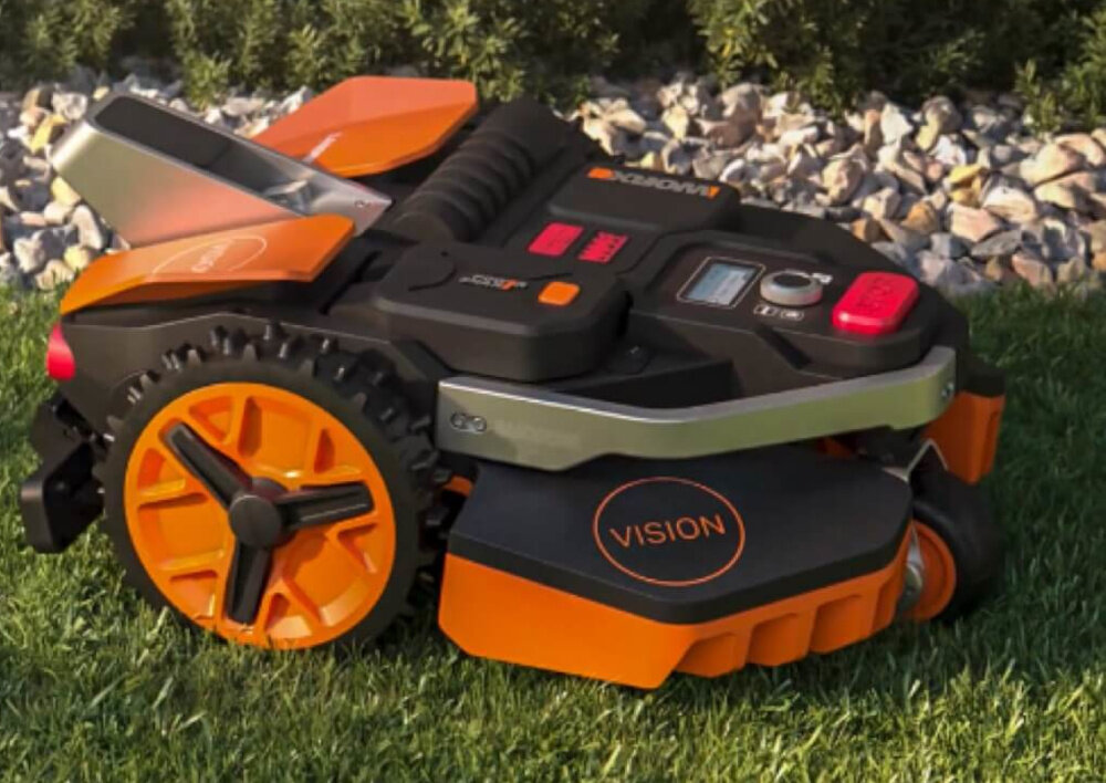 Robot koszący WORX Landroid Vision WR202E robot na trawie obok kamyki krzewy robot samodzielnie wraca do stacji dokującej czas ładowania około 115 minut automatyczne ładowanie