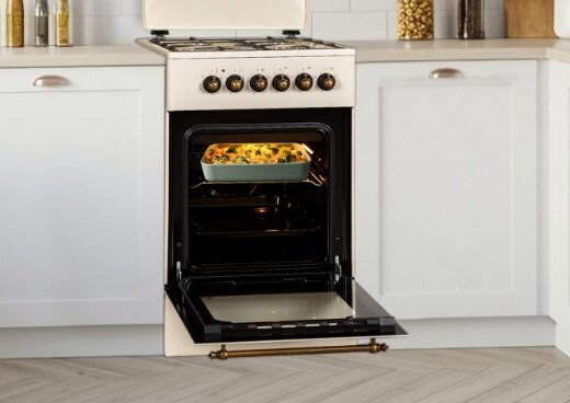 Kuchnia gazowo-elektryczna w zabudowie kuchennej z otwartym piekarnikiem. W środku piekarnika zapiekanka.