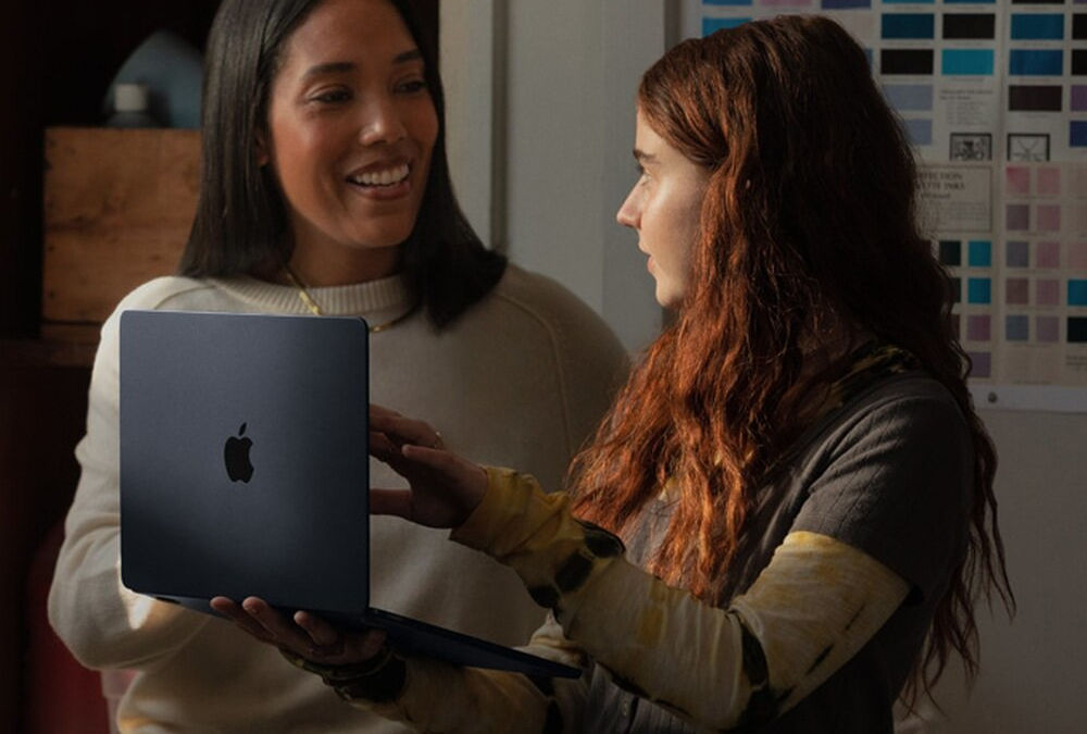 Laptop APPLE MacBook Air 2023 15.3 Retina M2 8GB RAM 512GB SSD macOS Gwiezdna szarość
					smukła i lekka konstrukcja, łączy elegancki wygląd z wysoką mobilnością,
					smukła obudowa z aluminium o grubości ok. 1,15 cm, waga ok. 1,51 kg,
					kobieta trzymająca laptop w trakcie rozmowy z drugą kobietą