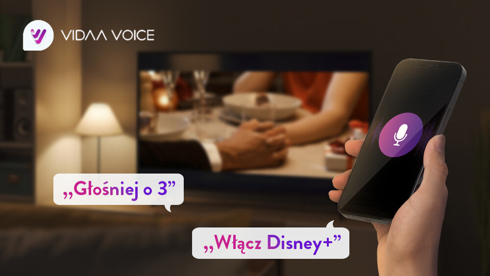 Telewizor JVC LT-50VD3500 - Szybkie sterowanie głosowe, telewizor stojący w salonie na stoliku, na pierwszym planie jest ręka z telefonem przedstawiający sterowanie głosowe