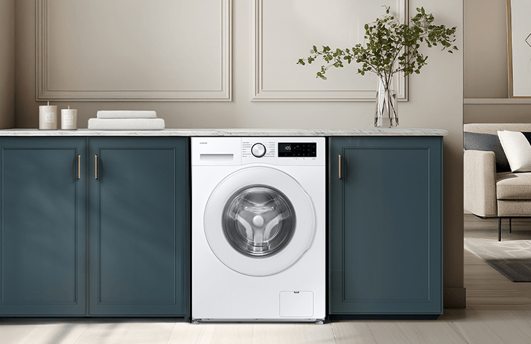 Pralka w zabudowie kuchennej z białym frontem i czarnym panelem sterowania. Obok znajdują się szafki z ciemnymi frontami i blatem marmurowym, a na blacie stoi wazon z zielonymi gałązkami.