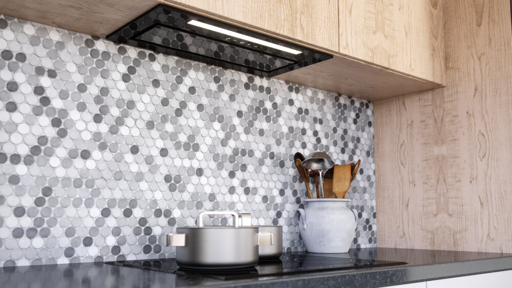 Kuchnia z okapem wbudowanym w szafkę nad płytą grzewczą, na której stoi garnek. Ściana wyłożona jest mozaikowymi płytkami w odcieniach szarości, a obok znajduje się pojemnik z przyborami kuchennymi.