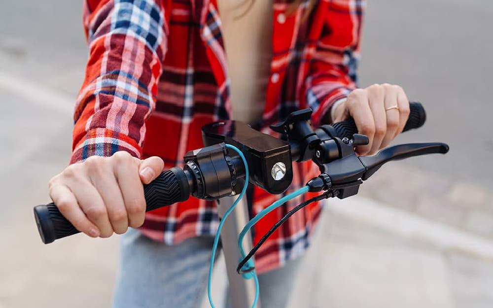 Hulajnoga elektryczna MOTUS Scooty 10 Lite Gen 4 30km 350W Amortyzacja 10 cali Szary zbliżenie na kierownicę osoba trzyma kierownicę widok na przednie światło bezpieczeństwo przednie i tylne światła kierunkowskazy