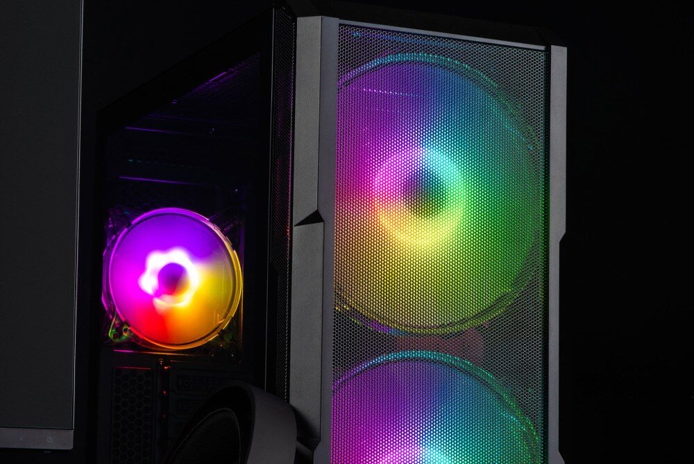 Komputer MAD DOG Fortnite Ready FR-02WR32WPV2 Ujęcie komputera w czarnej obudowie z podświetlanymi wentylatorami. Sprzęt stoi na biurku, obok znajduje się monitor. Boczny panel ze szkła hartowanego odsłania wnętrze obudowy, obudowa, wentylacja, porty, filtry, szklany bok