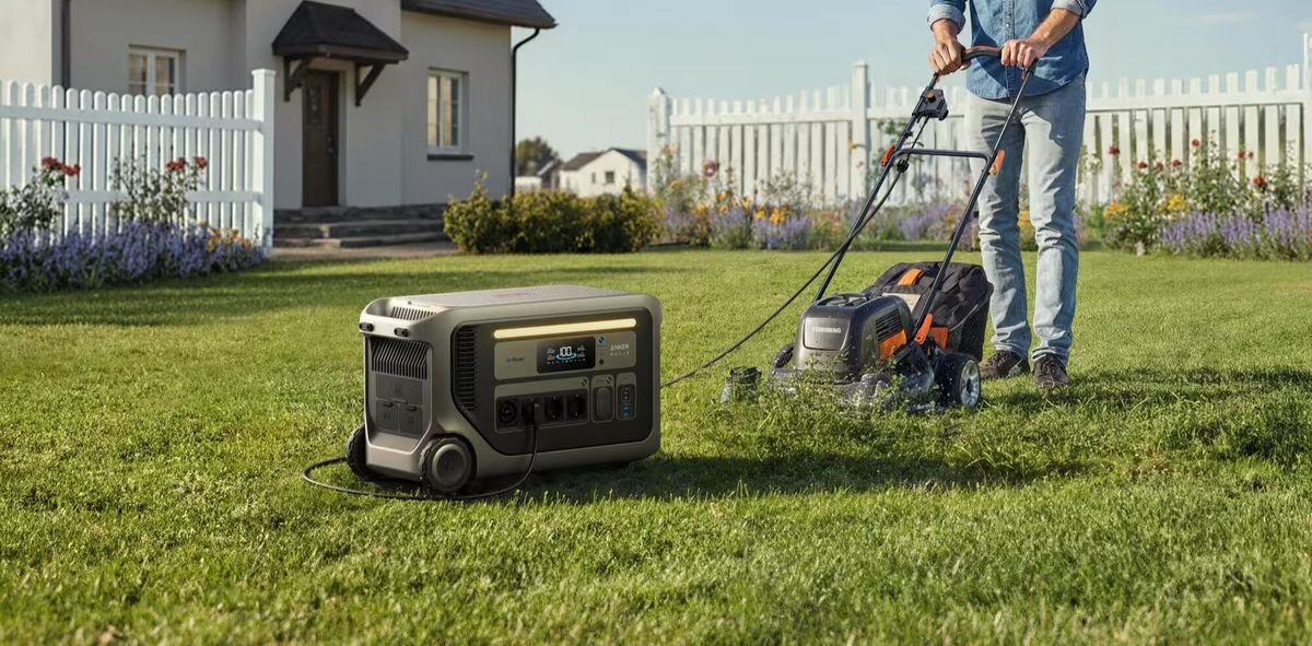 Samochód elektryczny jest podłączony do stacji zasilania stojącej na zewnątrz budynku. Stacja zasilania ma wyświetlacz i kilka gniazd do podłączenia urządzeń.