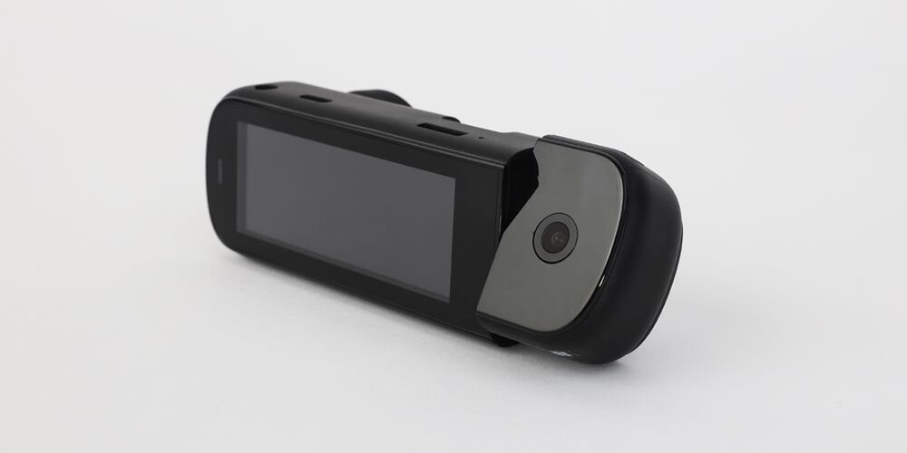 Na obrazie widoczny jest czarny wideorejestrator z ekranem i kamerą. Urządzenie ma nowoczesny design i jest ustawione na białym tle.