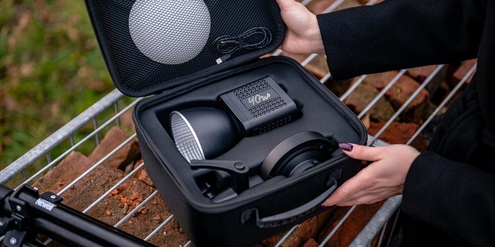 Lampa LED Newell Tara 40 RGB wraz z akcesoriami z zestawu w etui. Obok na metalowej kratce leży złożony statyw.