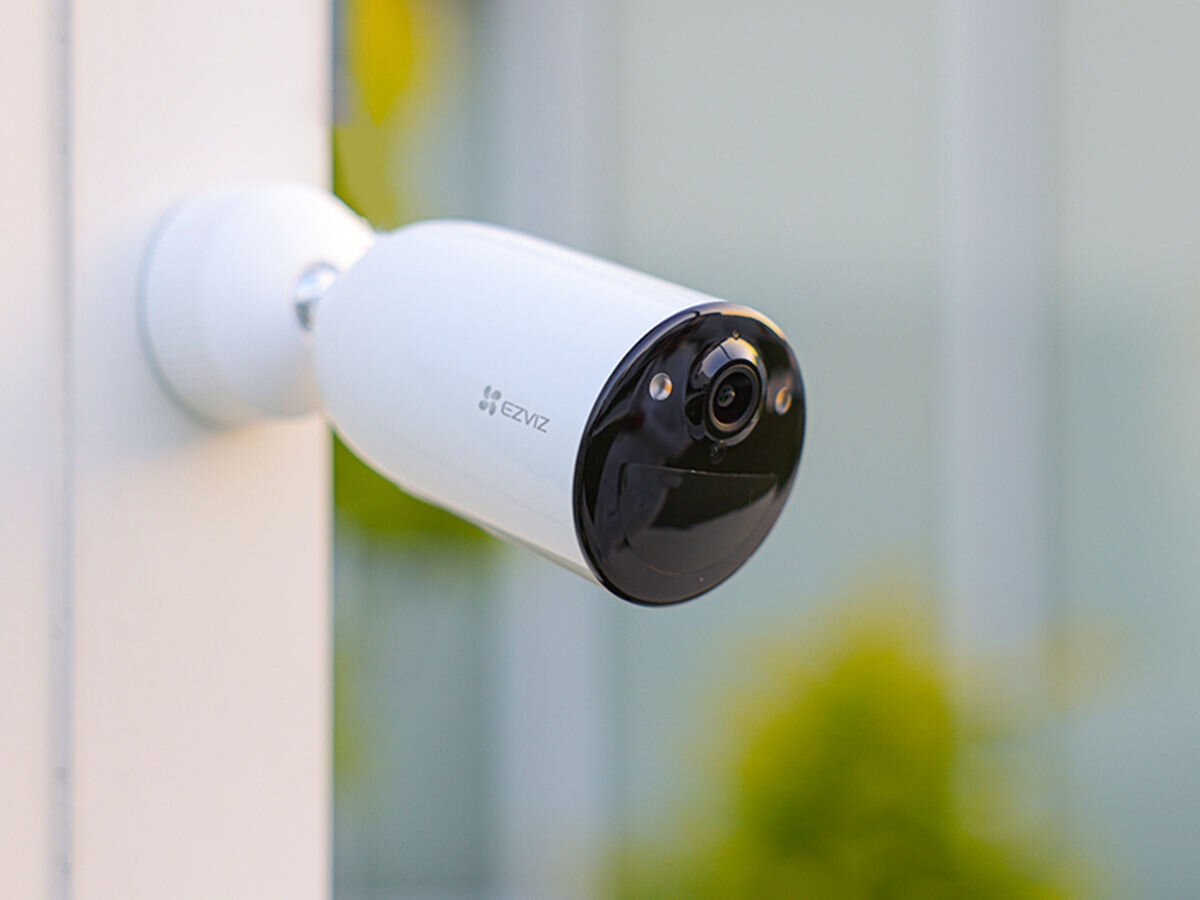 Kamera EZVIZ CB3 Zewnętrzna, Wi-Fi, skuteczna, ochrona, obsługa, kompatybilny, Zbliżenie na nowoczesną kamerę EZVIZ zamontowaną na białej ścianie, rozmyte zielone tło